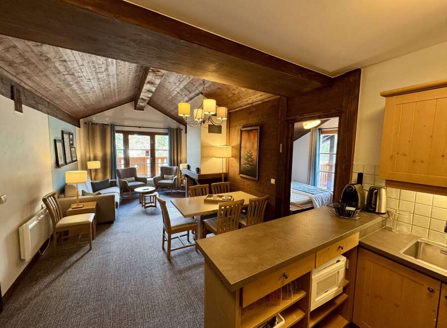 Experience cozy living in this charming mountain retreat, featuring a rustic wood-paneled interior and a vaulted ceiling with exposed beams.