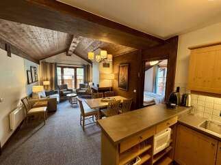 Experience cozy living in this charming mountain retreat, featuring a rustic wood-paneled interior and a vaulted ceiling with exposed beams.