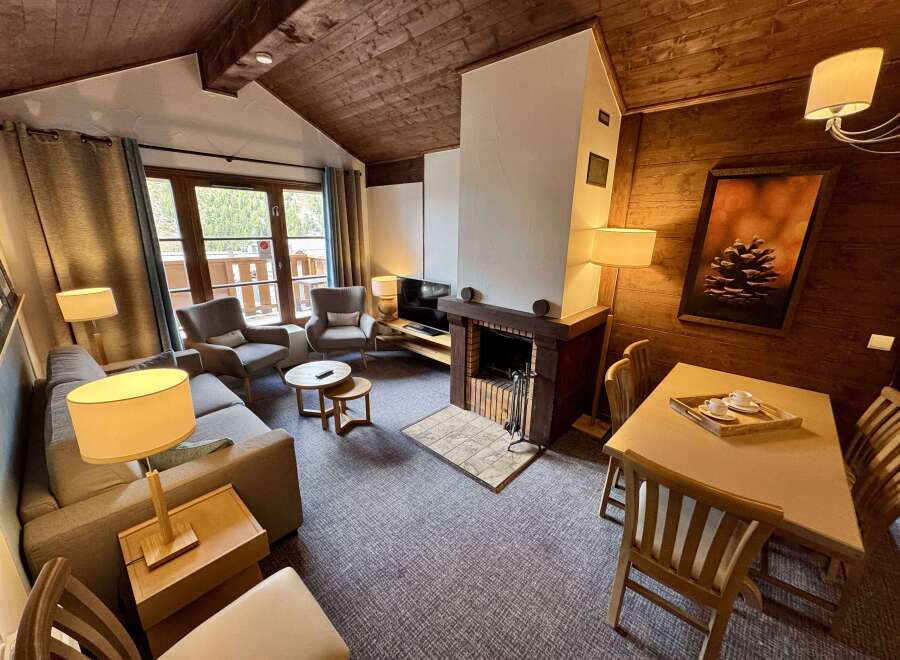 Experience cozy mountain living in this charming living room, featuring a rustic wood-paneled ceiling and a striking stone fireplace.