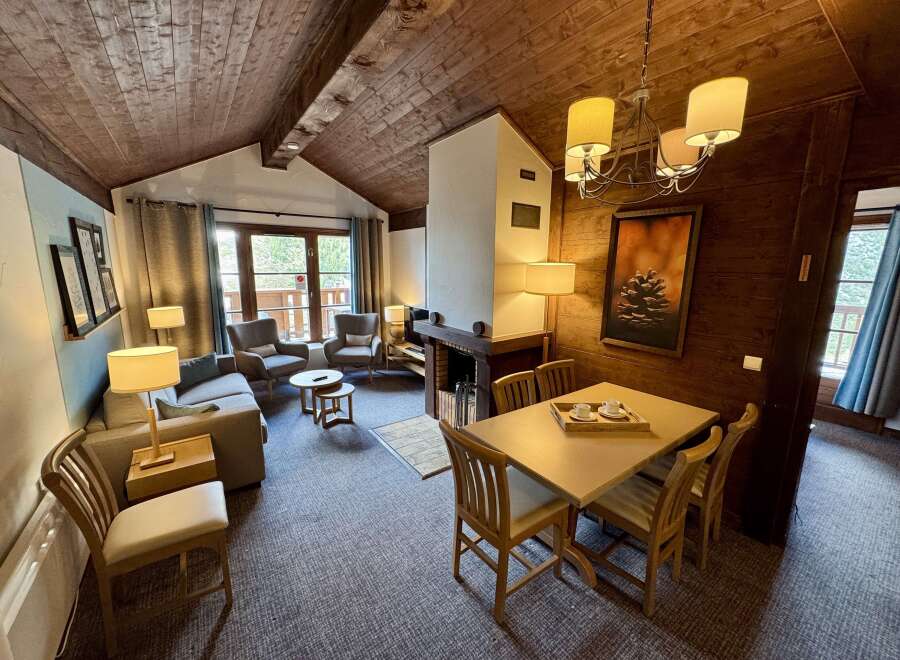 Experience cozy living in this charming mountain retreat, featuring a rustic wood-paneled ceiling and a warm fireplace.