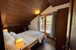 Experience cozy mountain living in this charming bedroom featuring a comfortable bed, warm wood-paneled walls, and a private balcony accessed through French doors.