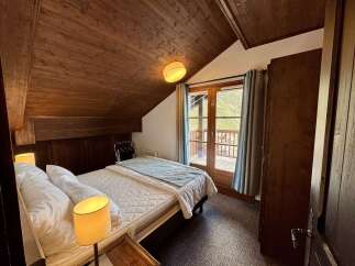 Experience cozy mountain living in this charming bedroom featuring a comfortable bed, warm wood-paneled walls, and a private balcony accessed through French doors.