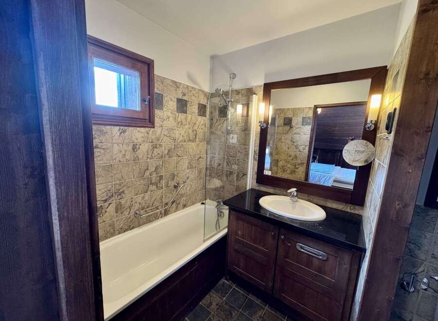 This charming bathroom features a classic white bathtub with a chrome grab bar and a glass shower screen, perfect for relaxing after a long day.