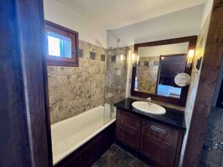 This charming bathroom features a classic white bathtub with a chrome grab bar and a glass shower screen, perfect for relaxing after a long day.