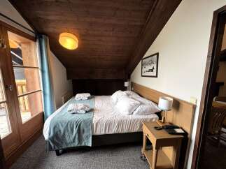 Experience rustic charm in this cozy hotel room featuring a comfortable bed adorned with plush white linens and two neatly folded bathrobes.