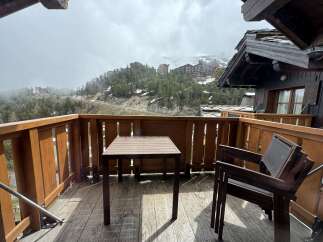 Enjoy breathtaking mountain views from this charming wooden balcony, complete with a table and chairs.