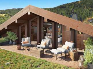 Experience luxury mountain living with this stunning chalet featuring a spacious wooden deck overlooking a lush green landscape and a forest-covered mountain.