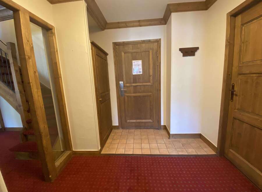 Step into a warm and inviting entryway featuring rich wooden doors and trim, complemented by a classic red carpet.