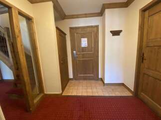Step into a warm and inviting entryway featuring rich wooden doors and trim, complemented by a classic red carpet.