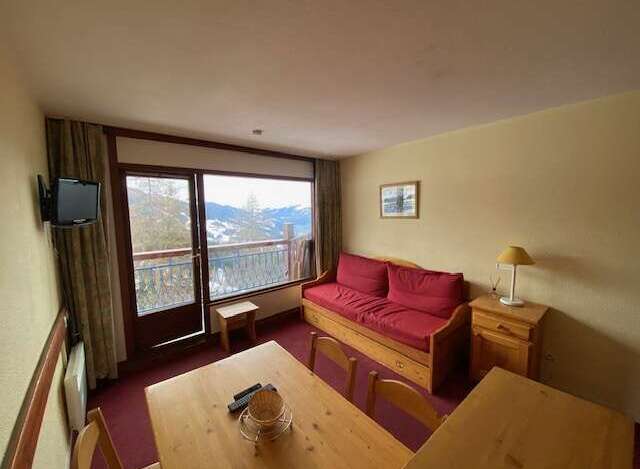 Enjoy stunning mountain views from this cozy living area, complete with a comfortable red sofa and a large window overlooking a scenic balcony.