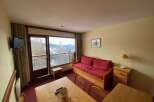 Enjoy stunning mountain views from this cozy living area, complete with a comfortable red sofa and a large window overlooking a scenic balcony.