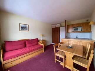 This charming studio apartment features a comfortable living area with a red sofa, perfect for relaxing after a day of skiing.