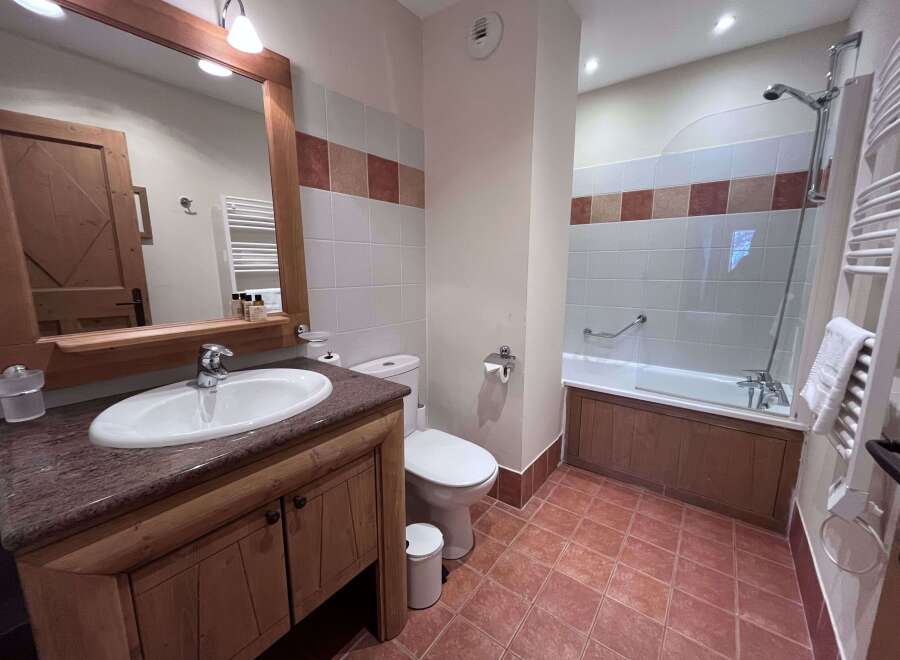 This charming bathroom features a spacious vanity with a granite countertop and ample storage, complemented by a large mirror with integrated lighting.