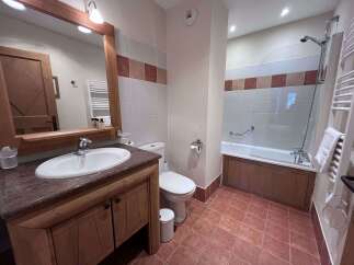 This charming bathroom features a spacious vanity with a granite countertop and ample storage, complemented by a large mirror with integrated lighting.