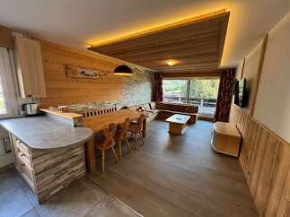 Experience cozy living in this charming mountain retreat, featuring a spacious open-plan living and dining area with a rustic wooden ceiling and ambient lighting.