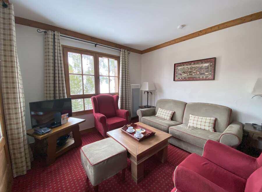 Experience cozy living in this charming living room, featuring a plush red armchair and a comfortable sofa perfect for relaxation.