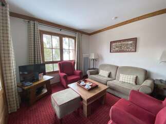 Experience cozy living in this charming living room, featuring a plush red armchair and a comfortable sofa perfect for relaxation.