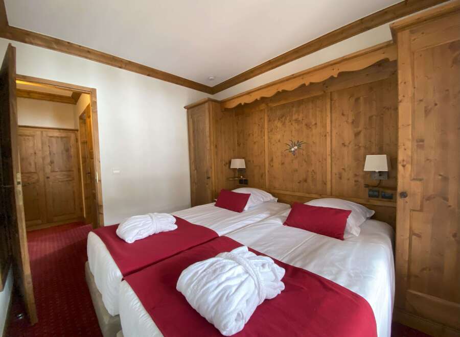 Experience alpine charm in this inviting hotel room, featuring two comfortable twin beds adorned with plush red throws and white bathrobes.