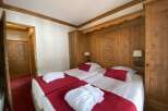 Experience alpine charm in this inviting hotel room, featuring two comfortable twin beds adorned with plush red throws and white bathrobes.