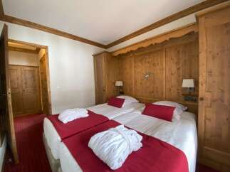 Experience alpine charm in this inviting hotel room, featuring two comfortable twin beds adorned with plush red throws and white bathrobes.