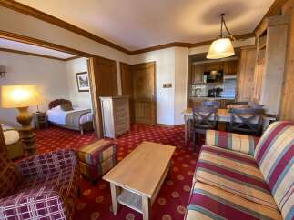 Discover this charming hotel room featuring a cozy sleeping area with two beds and a separate living space with a comfortable sofa and armchair.