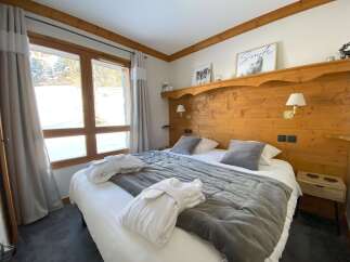 Experience ultimate comfort in this cozy bedroom, featuring a plush king-sized bed adorned with soft grey linens and two inviting bathrobes.