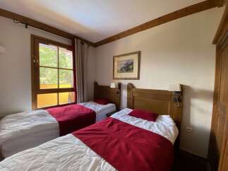 This charming bedroom features two comfortable twin beds, each adorned with crisp white linens and a striking red throw blanket.