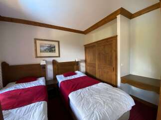 This charming hotel room features two comfortable twin beds, each adorned with crisp white linens and a vibrant red throw blanket.