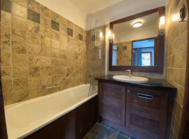 This charming bathroom features a spacious bathtub with a grab bar, perfect for a relaxing soak.