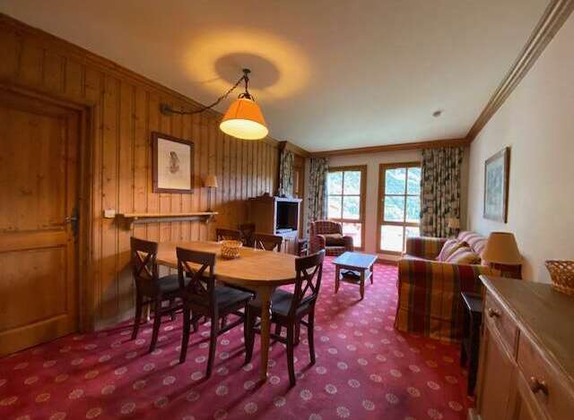 Experience cozy living in this charming mountain retreat, featuring a warm wood-paneled dining area with a rustic chandelier and comfortable seating.
