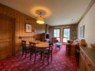 Experience cozy living in this charming mountain retreat, featuring a warm wood-paneled dining area with a rustic chandelier and comfortable seating.