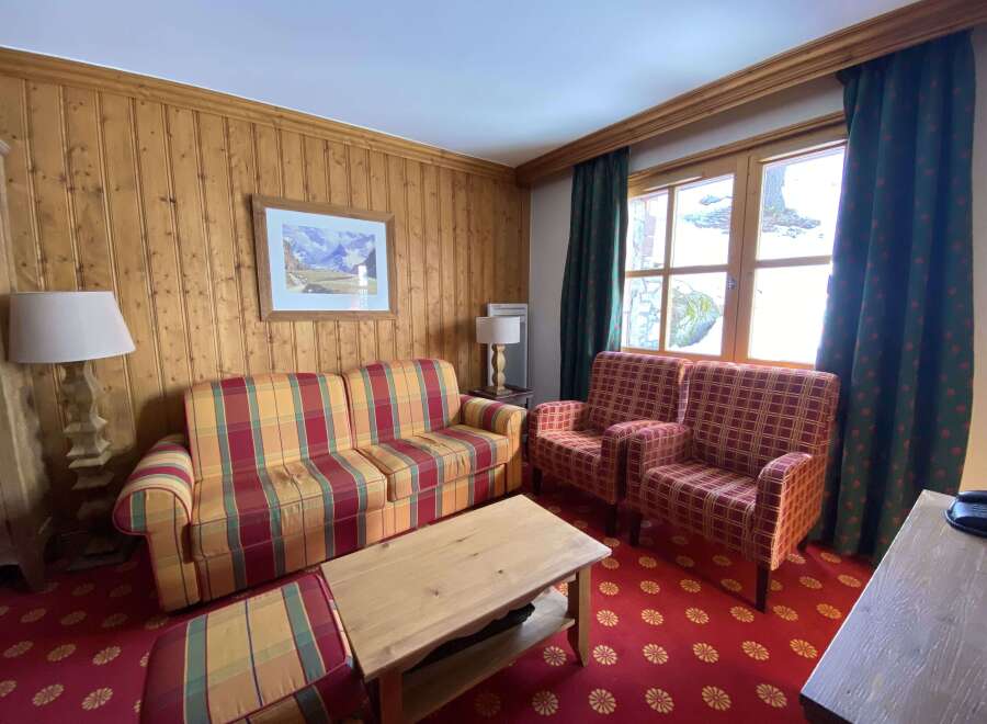 Experience cozy mountain living in this charming room featuring warm wood paneling and a vibrant plaid sofa and armchairs.