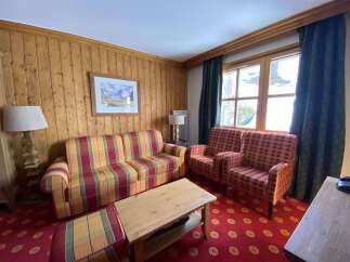 Experience cozy mountain living in this charming room featuring warm wood paneling and a vibrant plaid sofa and armchairs.