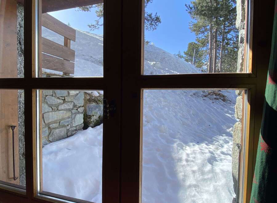 Experience breathtaking mountain views from this cozy cabin, featuring large windows that showcase a pristine snowy landscape.