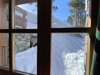 Experience breathtaking mountain views from this cozy cabin, featuring large windows that showcase a pristine snowy landscape.