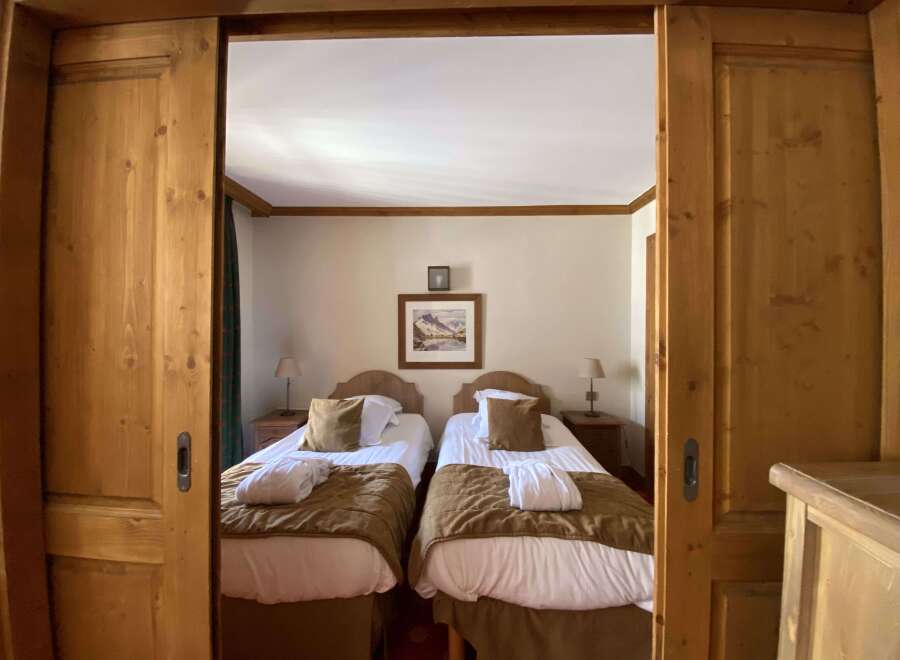 Experience alpine charm in this cozy bedroom featuring two inviting twin beds, each adorned with plush brown throws and crisp white linens.