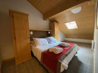 Experience cozy mountain living in this charming attic bedroom, featuring a comfortable queen-size bed adorned with plush white linens and a festive red runner.