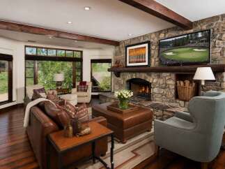 Experience luxury mountain living in this stunning living room, featuring a grand stone fireplace and expansive windows offering breathtaking natural views.