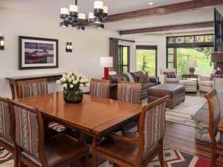 Experience luxurious mountain living in this stunning dining and living area, featuring a beautiful wooden dining table with upholstered chairs and a cozy seating arrangement by the fireplace.