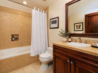 This charming bathroom features a warm and inviting ambiance with its tan tiled shower and tub surround.