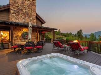 Experience luxury mountain living with this stunning deck featuring a bubbling hot tub and a cozy fire pit, perfect for enjoying breathtaking sunset views.