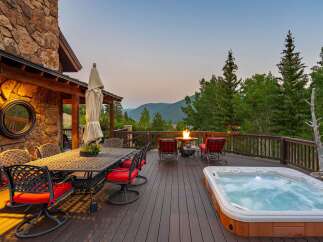 Experience luxury mountain living on this expansive deck, complete with a bubbling hot tub and a cozy fire pit, perfect for enjoying breathtaking sunset views.