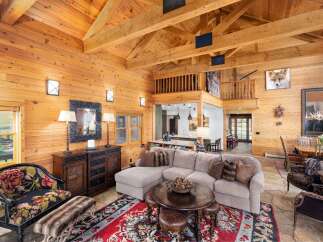 Experience rustic luxury in this stunning log cabin living room, featuring a grand vaulted ceiling with exposed wooden beams and a cozy stone fireplace.