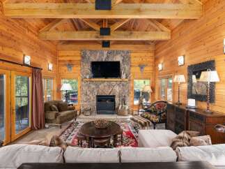 Experience rustic luxury in this stunning log cabin living room, featuring a grand stone fireplace and exposed wooden beams.