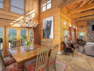 Experience rustic elegance in this stunning log cabin dining room, featuring a grand antler chandelier and a captivating bear artwork.