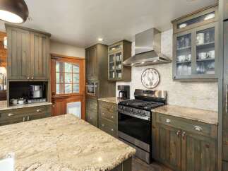 This rustic kitchen features distressed green cabinetry with glass-front upper cabinets displaying glassware and mugs.
