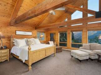 Experience rustic luxury in this stunning log cabin bedroom, featuring a grand wooden bed and vaulted ceilings with exposed beams.