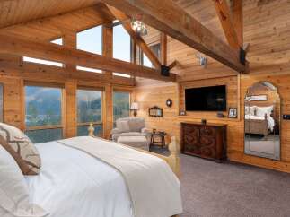 Experience rustic luxury in this stunning log cabin bedroom, featuring a vaulted wood-paneled ceiling with exposed beams and a breathtaking mountain view through expansive windows.