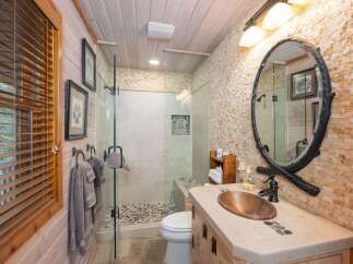 Experience rustic charm in this beautifully appointed bathroom, featuring a unique copper vessel sink and a spacious walk-in shower with pebble flooring.