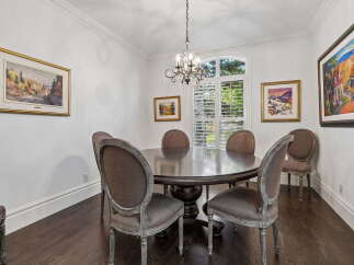 This elegant dining room features a large, dark wood round dining table surrounded by upholstered chairs with distressed wood frames.